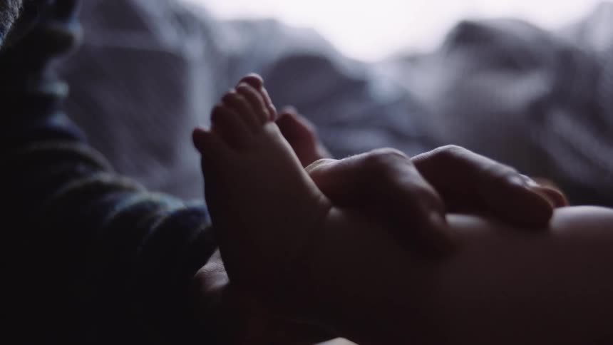 A person grabs the leg of a baby laying in bed at home