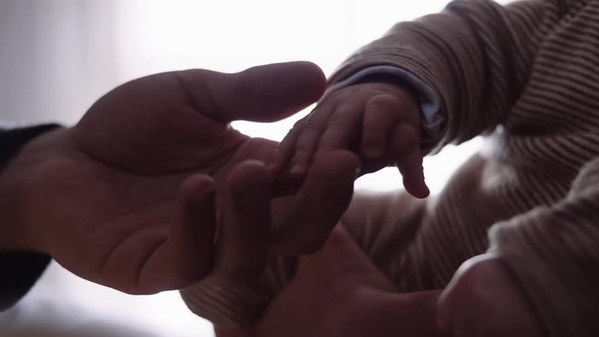 An infant in a striped shirt grabs onto his fathers index finger