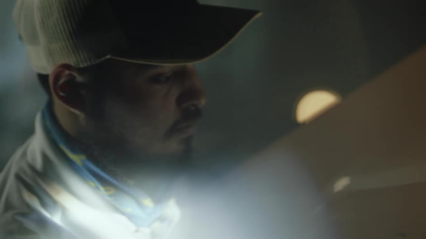 A man with a hat wiping a car headlights with a cloth