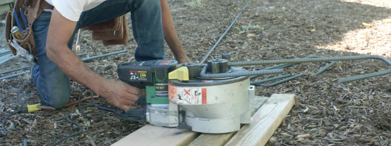 A man is bending rebar in the yard with a tool