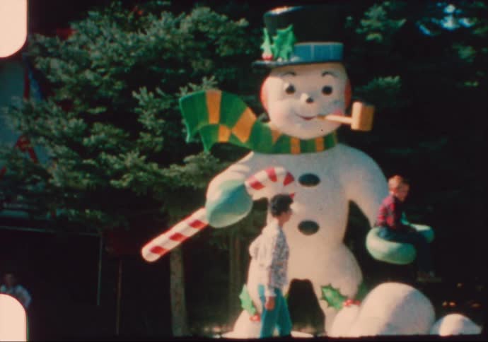 Children play on a snowman statue in a park decorated for Christmas in the 1950's