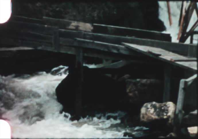 A small river rushes down through cascading rocks under a bridge