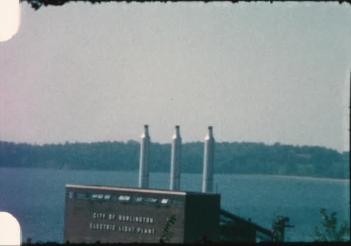 A factory with chimneys near a river with trees the sky and clouds in the background