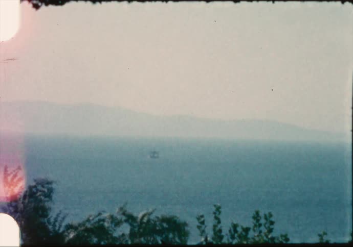 Trees in the foreground with a lake with a mountain range the sky and clouds in the background
