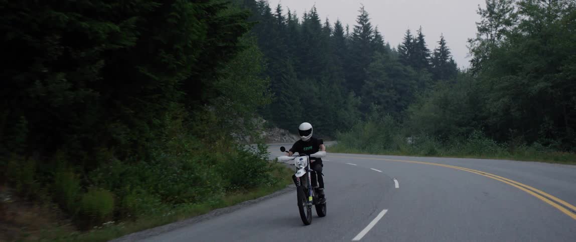 A motorcyclist rides a dirt bike along a road through a forest during the day