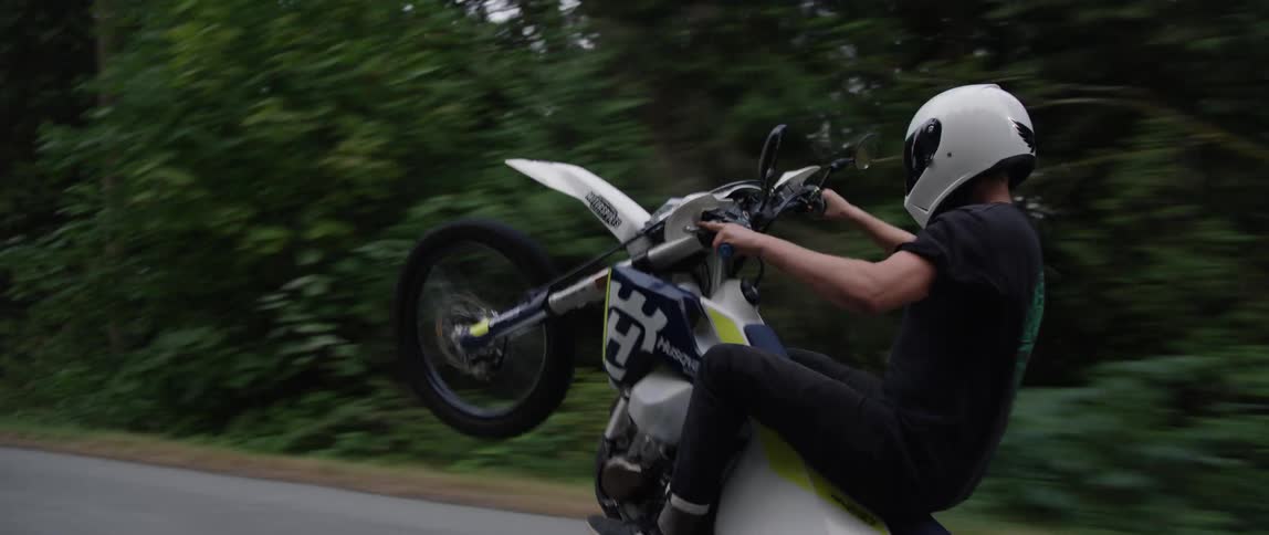 Motorcyclist riding a wheelie on a road through the woods