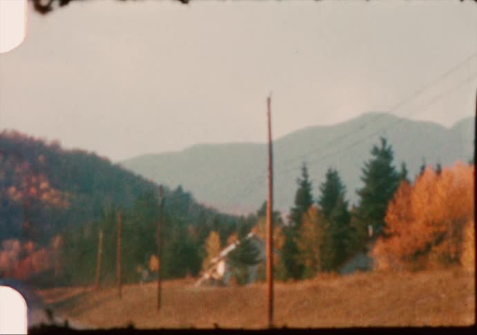 A car travels on a rural road with hills and trees brightly colored foliage