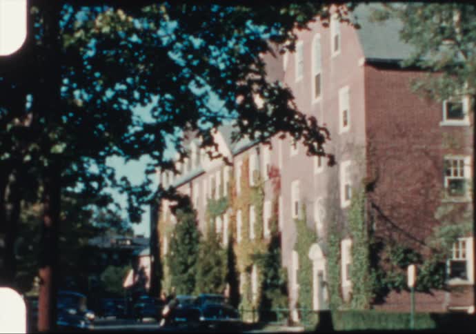 Ivy climbs tall brick buildings on a quiet city street in the 1950's
