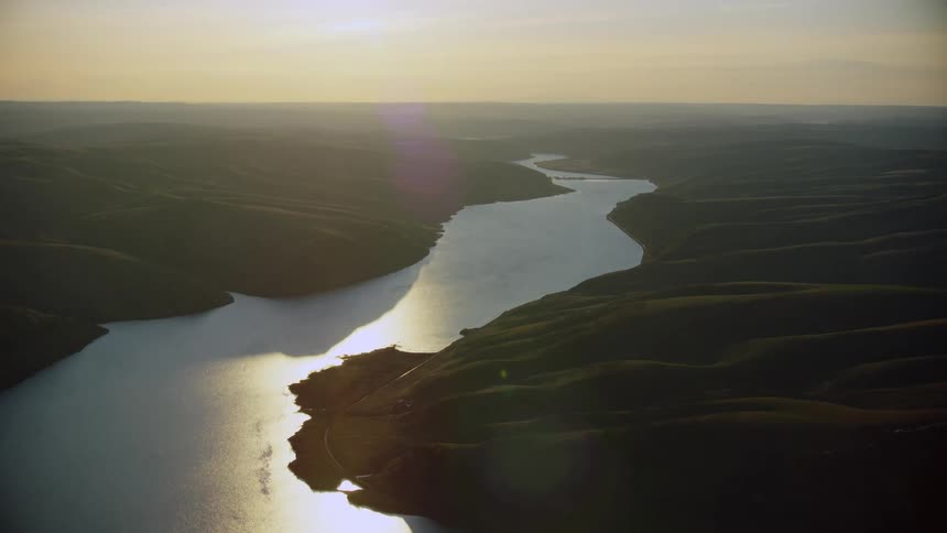 Little Goose Dam is seen far on the horizon as the setting sun casts golden hour reflective light on the Lower Snake River in the Western United States