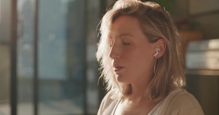 Blonde pregnant woman sits on the floor and wears headphones to relax in the living room at home