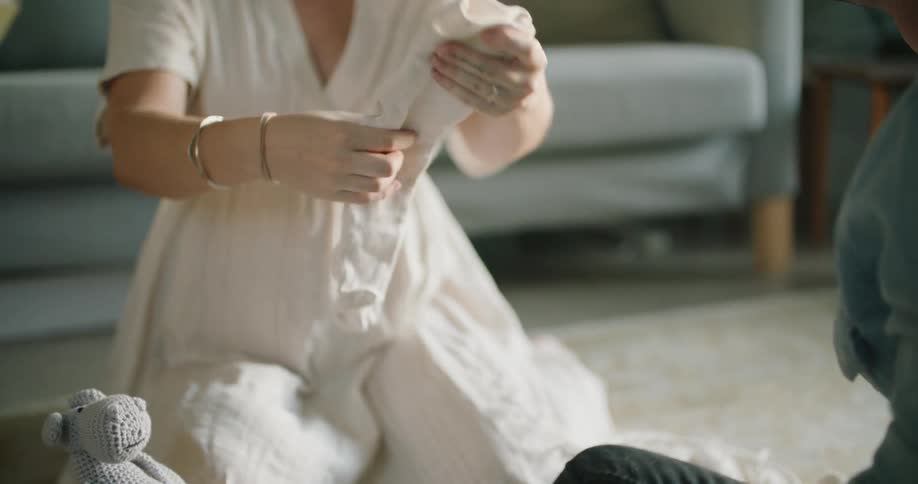 A pregnant woman sitting on the floor holding baby clothing while talking to a man