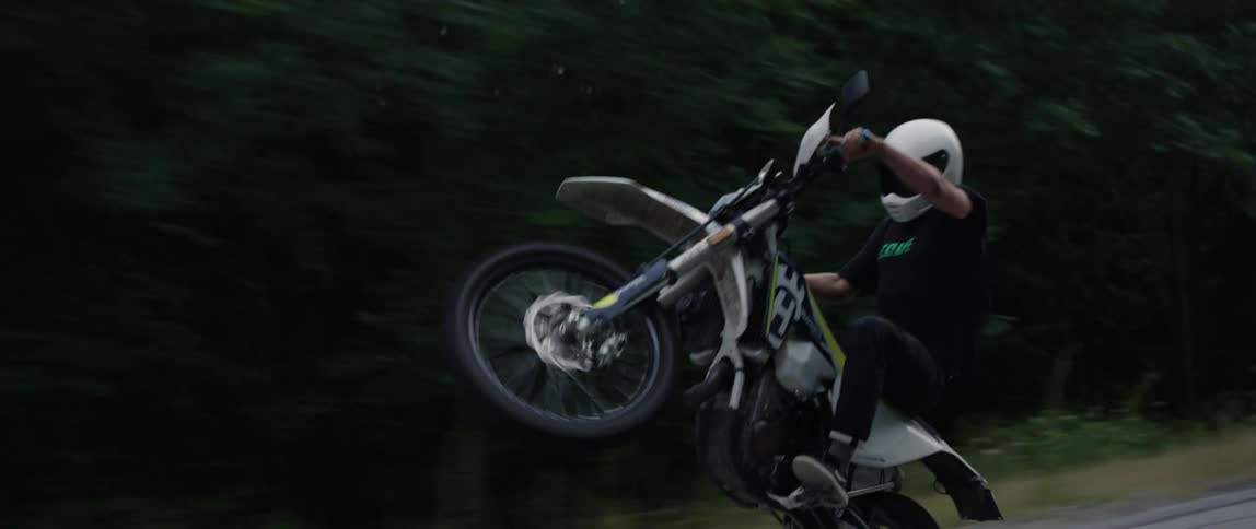 Motorcyclist riding a wheelie on a road in the woods
