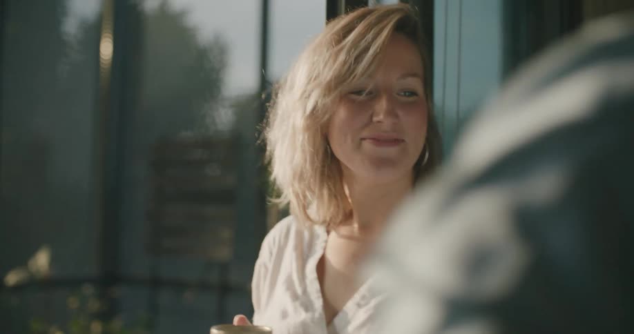 Pregnant woman wearing a white dress drinks a hot beverage at home while kissing her husband goodbye
