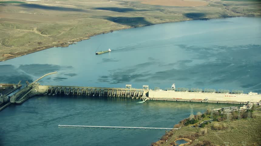 The John Day Dam on the Columbia River with a barge moving freight down the Columbia River as seen high above in this aerial in evening warm light