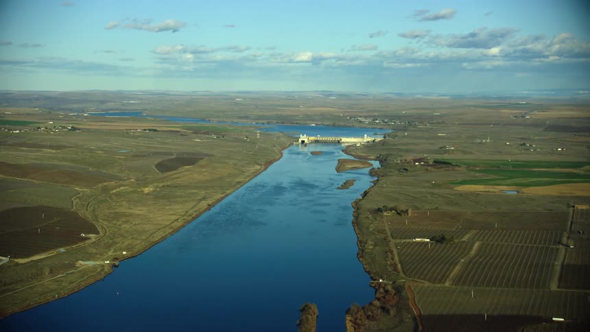 Looking upstream at Ice Harbor Dam in Eastern Washington on a clear sunny day with agricultural land on both sides of the river