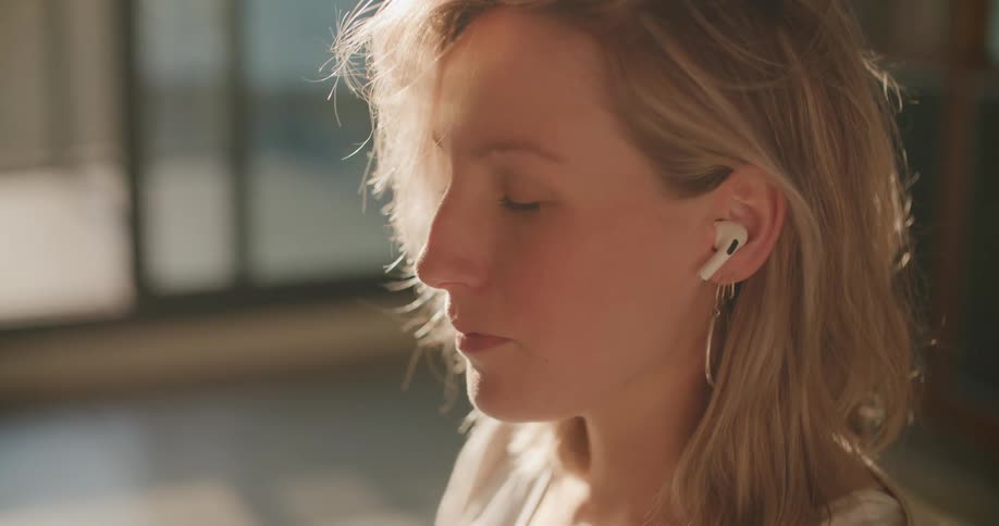 A woman opens her eyes and smiles while meditating at home with earbuds in