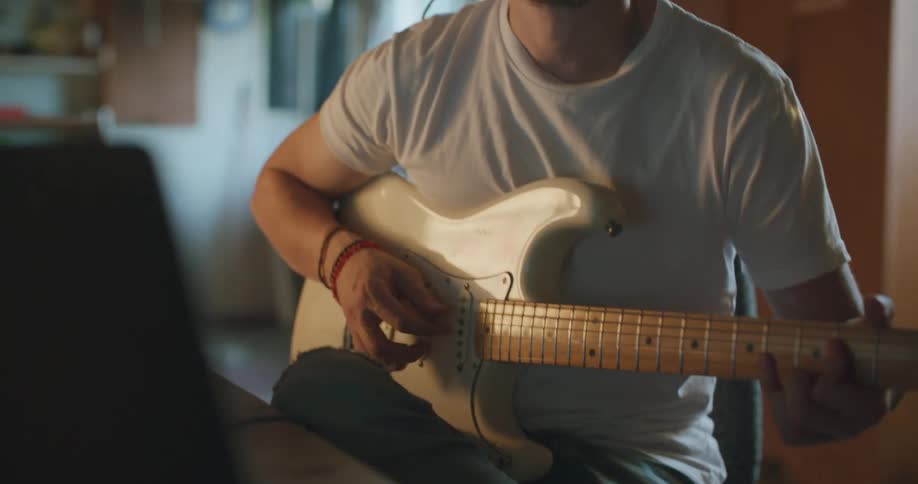 A man with a headphones and guitar sitting in front of a laptop