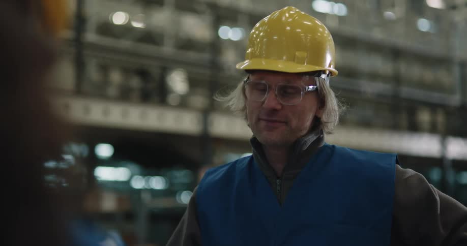 A man with a hardhat and vest in a warehouse with shelves in the background