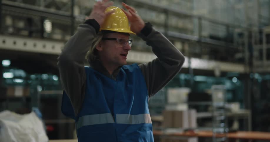 A man with a hardhat and a vest in a warehouse shaking a man and womans hand