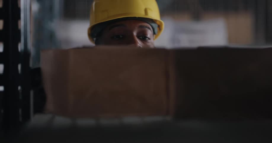 A man with a hardhat and gloves scanning a box and removing it from a shelf in a warehouse