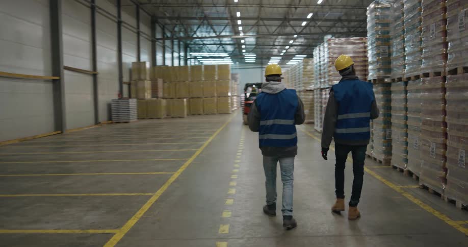 Workers walking along the pallets of products stored inside a warehouse