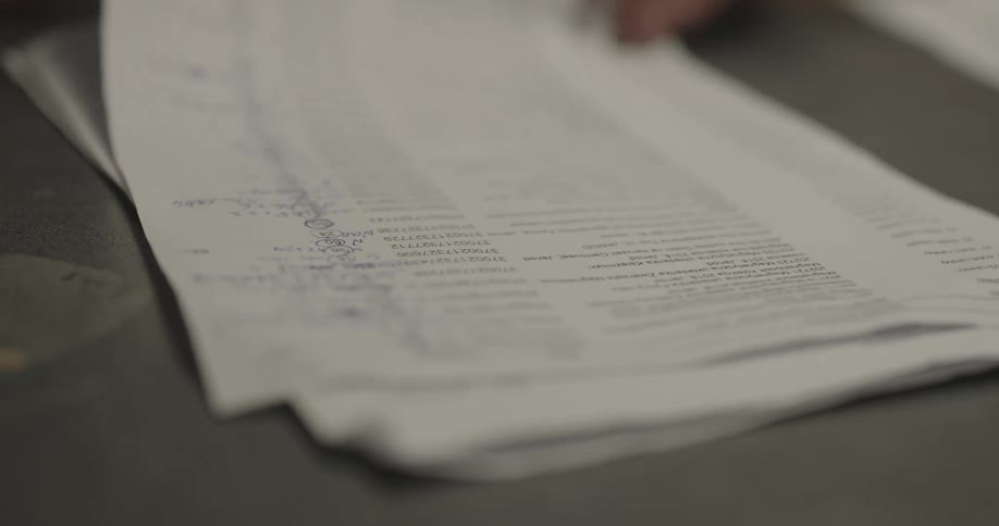 A woman quickly scrolls down sheets of typed paper with a pencil