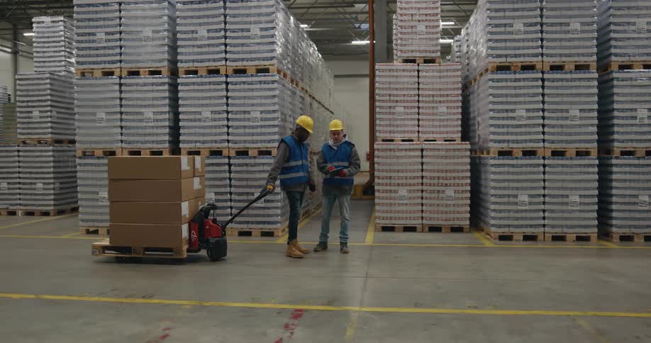 Worker carrying a forklift stops to talk to a coworker inside a warehouse