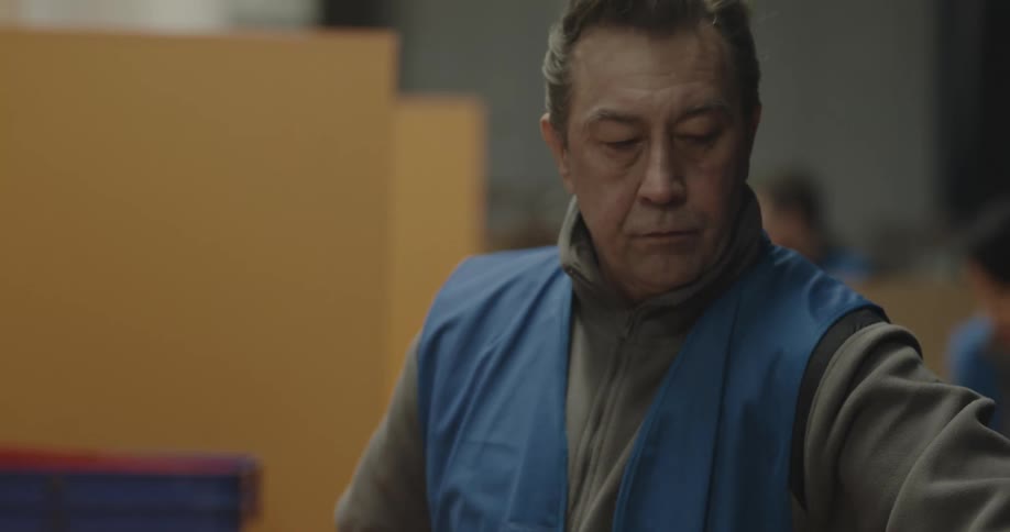 A man in a warehouse with a vest taping a box with tape