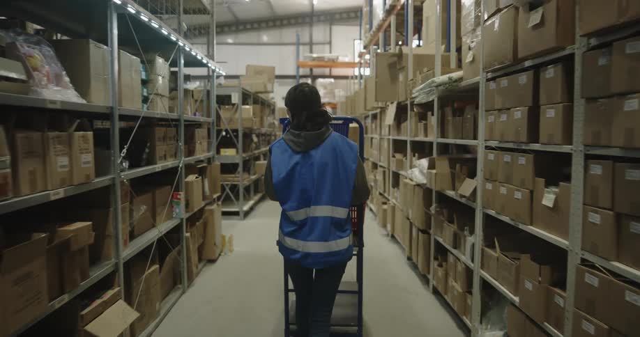 A woman walking around a warehouse with a cart