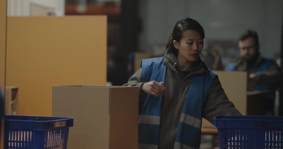 A woman with a vest in a warehouse packing a box with plastic
