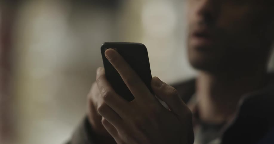 Male worker with yellow hard hat looks up and uses smartphone