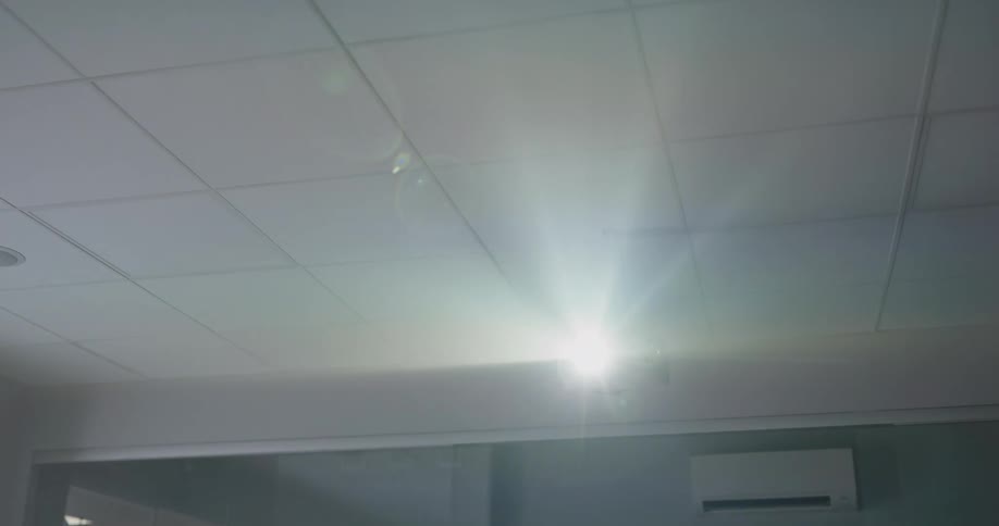 A room with a projector on the ceiling with a wall and a doorway in the background