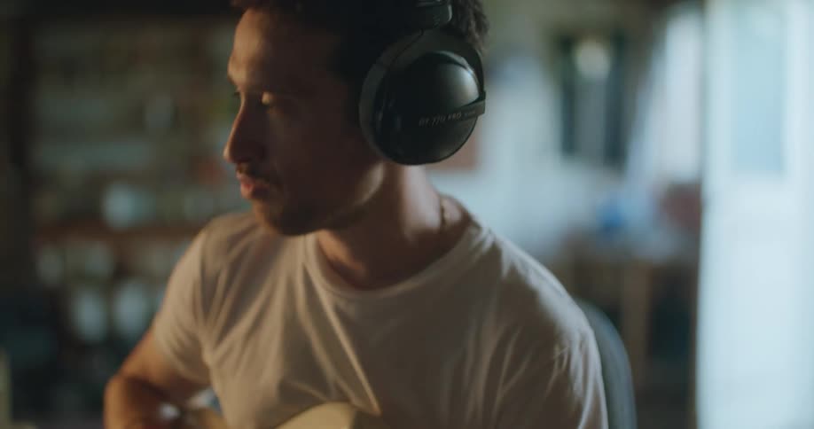 A man is sitting in his house and playing guitar