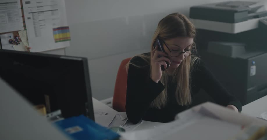 A woman is sitting at her desk talking on a cell phone