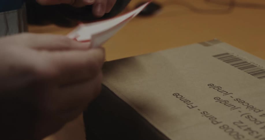 A person in a room peeling off a fragile sticker and placing it on a box on a table