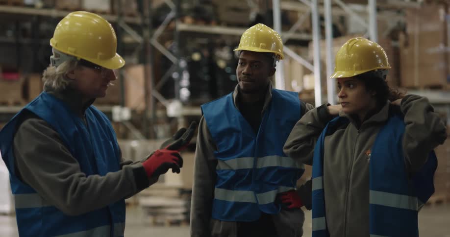 A man goes over procedures with warehouse employees as they don safety vests
