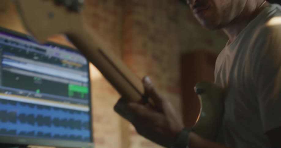 A man with a headphones playing the guitar in front of a computer at a desk
