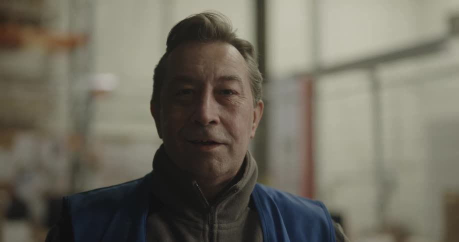 A man in a warehouse with a vest standing and staring