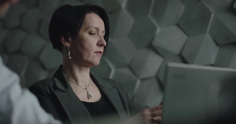 Businesswoman with short hair and a grey blazer talks on the smartphone during a business meeting