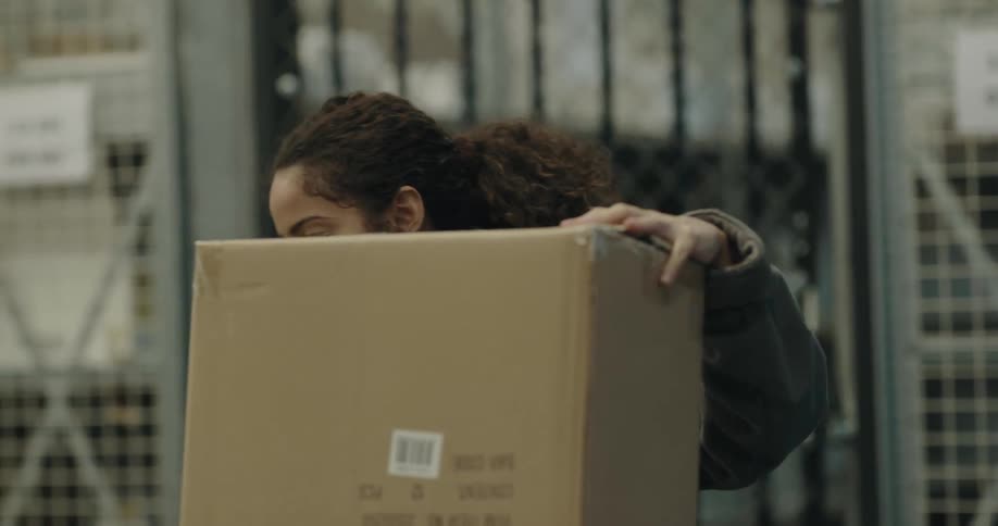 A woman and a man with vests in a warehouse while the woman folds a box