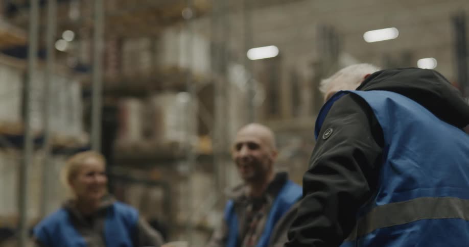 Men and women with vest in a warehouse with shelves in the background sitting and eating cookies