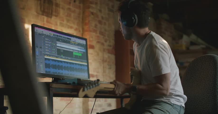 Musician recording an electric guitar session on a computer in a studio