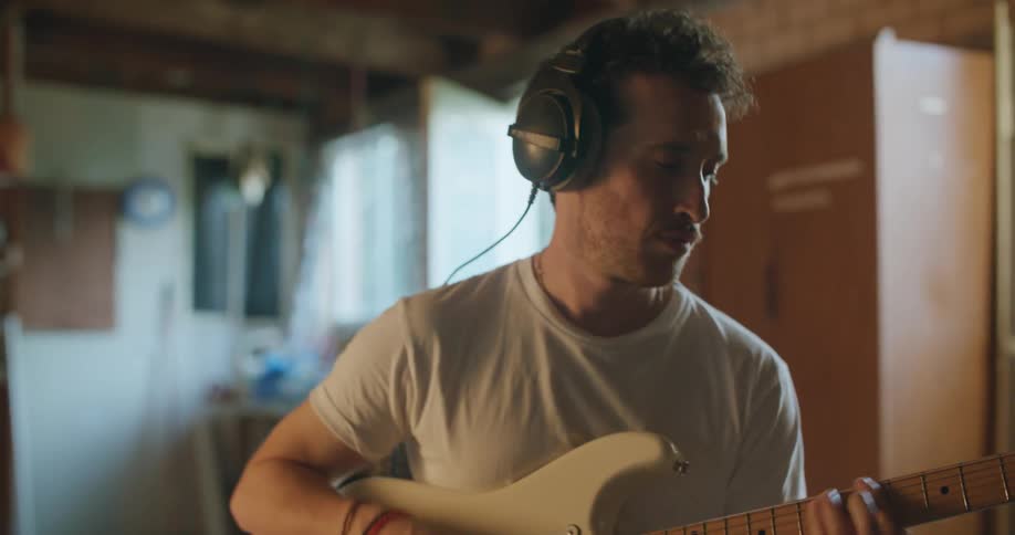 Man with black headphones a white t shirt and jeans plays electric guitar