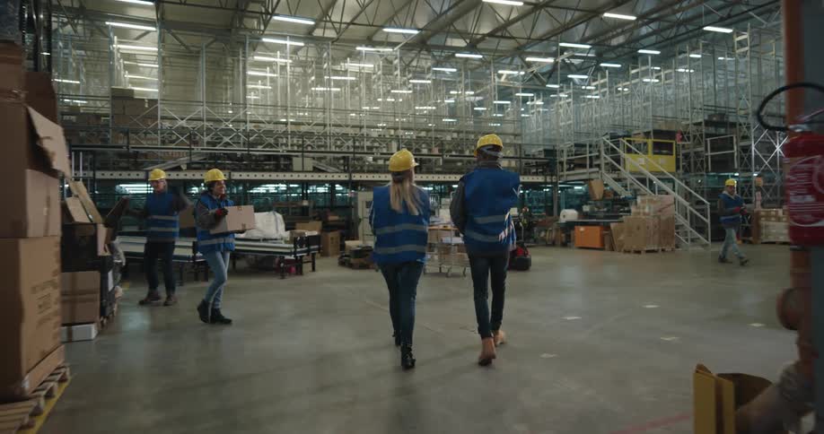 Workers in a warehouse wearing yellow hardhats checking inventory