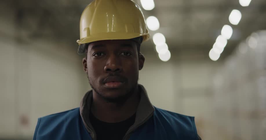 A man in a room with a hardhat with a wall and lights in the background