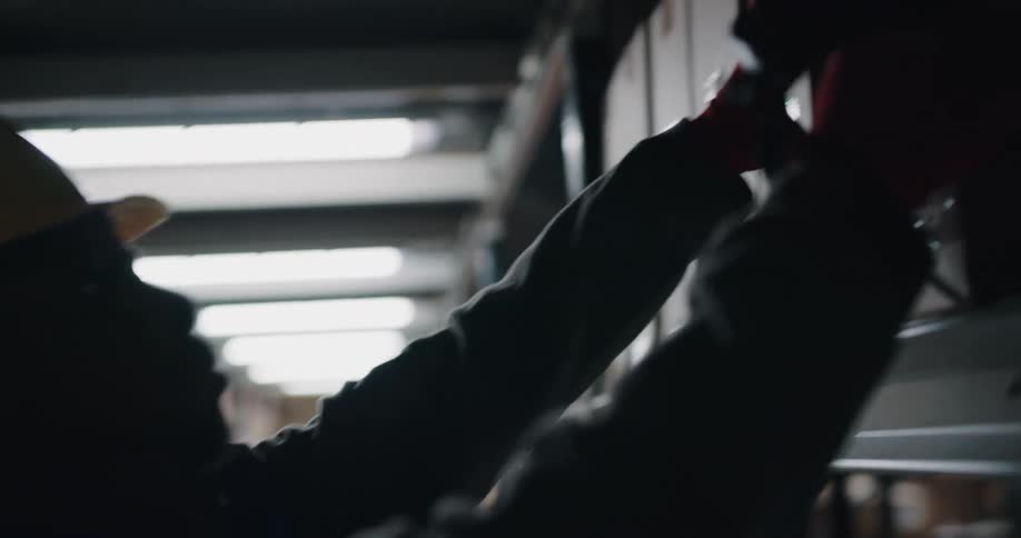 A male worker in a hard hat removing a box from a warehouse shelf
