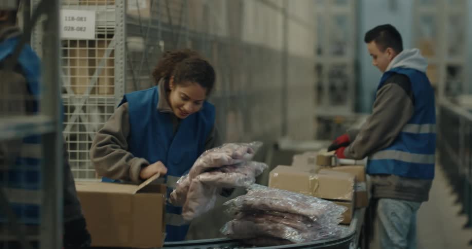 A woman smiles as one of her coworkers brings her more items to pack into boxes on the conveyor