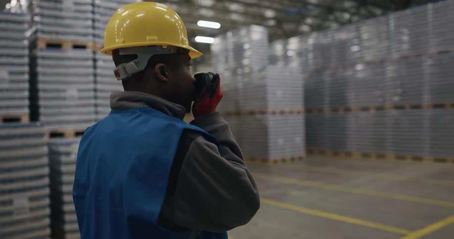 A man with a hardhat vest and gloves walking in a warehouse
