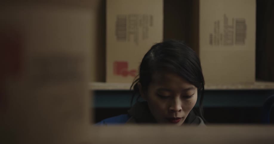 A woman picks up a box from a shelf and moves it