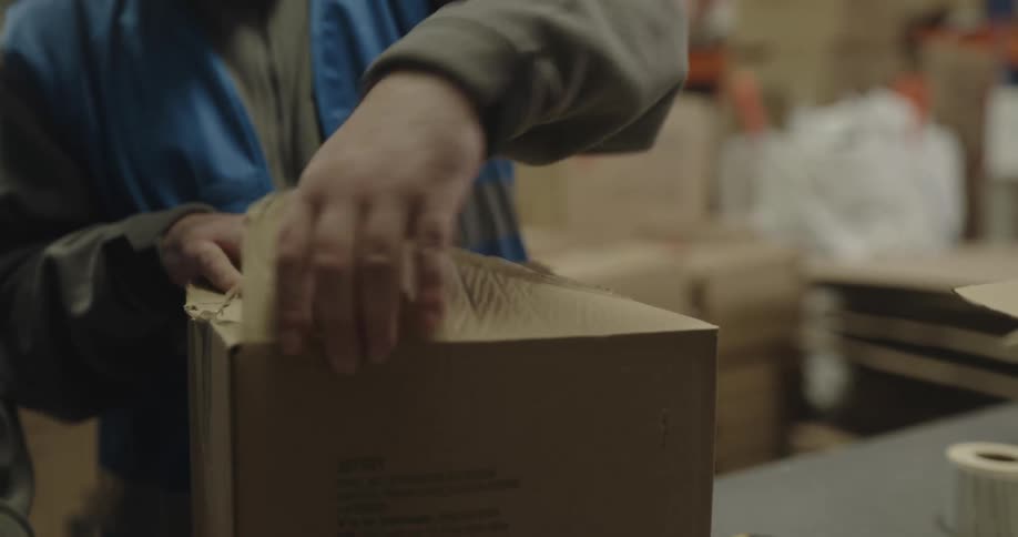 A man and a woman in a warehouse with the man opening a box with shelves in the background